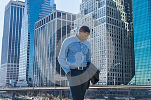 Young black man standing outdoors in business district in New York City, looking down, thinking