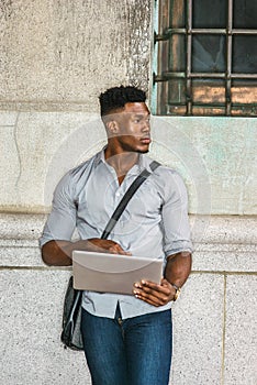 Young black man standing on street in New York City, working on laptop computer