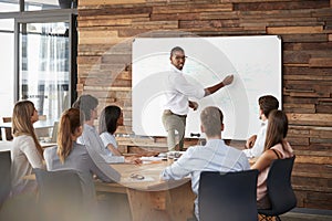 Young black man stands at whiteboard addressing team at meeting