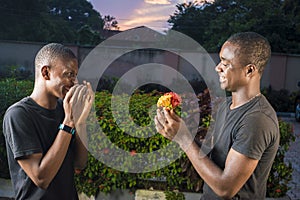 young black man surprises his gay partner with flowers outdoor, both laughing