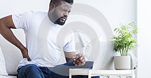 Young black man touching his sore back, working on laptop photo