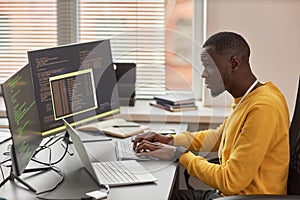 Young black man typing at keyboard and writing code in IT development company