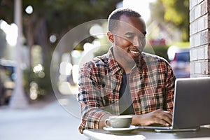 Young black man using a laptop computer outside a cafe photo