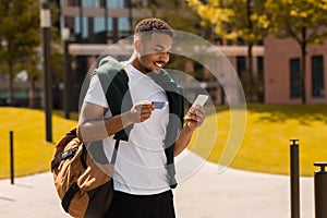Young black man using mobile phone and credit card, ordering food delivery or shopping online outdoors