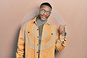 Young black man wearing casual clothes and glasses smiling with happy face looking and pointing to the side with thumb up