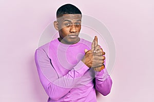 Young black man wearing casual pink sweater holding symbolic gun with hand gesture, playing killing shooting weapons, angry face