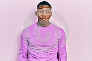 Young black man wearing casual pink sweater making fish face with lips, crazy and comical gesture