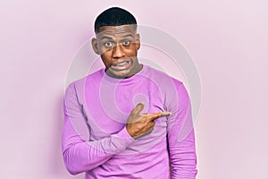 Young black man wearing casual pink sweater pointing aside worried and nervous with forefinger, concerned and surprised expression
