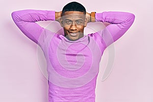 Young black man wearing casual pink sweater relaxing and stretching, arms and hands behind head and neck smiling happy