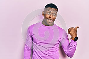 Young black man wearing casual pink sweater smiling with happy face looking and pointing to the side with thumb up