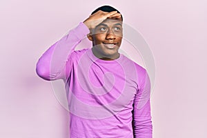 Young black man wearing casual pink sweater very happy and smiling looking far away with hand over head