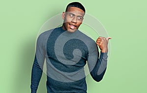 Young black man wearing casual sweater pointing thumb up to the side smiling happy with open mouth