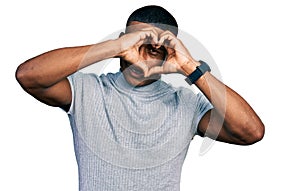 Young black man wearing casual t shirt doing heart shape with hand and fingers smiling looking through sign