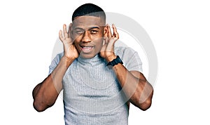Young black man wearing casual t shirt trying to hear both hands on ear gesture, curious for gossip