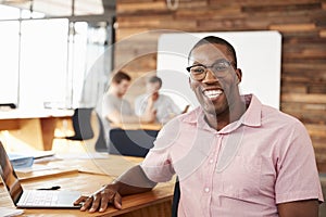 Young black man wearing glasses in office looking to camera