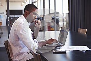 Young black man in wearing glasses using laptop in office