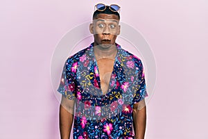 Young black man wearing hawaiian shirt and sunglasses making fish face with lips, crazy and comical gesture