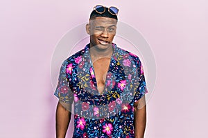 Young black man wearing hawaiian shirt and sunglasses winking looking at the camera with sexy expression, cheerful and happy face