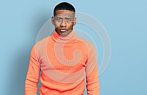 Young black man wearing orange turtleneck sweater with serious expression on face