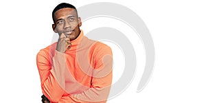 Young black man wearing orange turtleneck sweater serious face thinking about question with hand on chin, thoughtful about