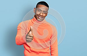 Young black man wearing orange turtleneck sweater smiling happy and positive, thumb up doing excellent and approval sign
