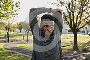 Young black man in sports clothing exhaling while doing stretches with arms raised in park photo
