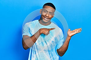 Young black man wearing tye die t shirt amazed and smiling to the camera while presenting with hand and pointing with finger