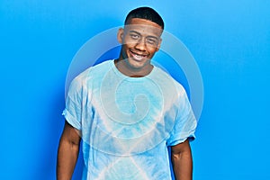 Young black man wearing tye die t shirt looking positive and happy standing and smiling with a confident smile showing teeth