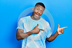 Young black man wearing tye die t shirt smiling and looking at the camera pointing with two hands and fingers to the side