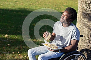 Young Black man in wheelchair having lunch in city park