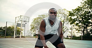 A young Black man in a white t-shirt shows how he skillfully handles a basketball on a basketball court outside in