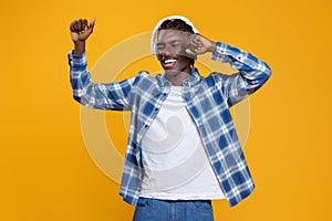 Young black man in wireless headphones enjoying music, dancing and smiling