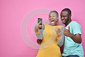 young black man and woman feeling excited and happy viewing content on a mobile phone together, giving thumbs up gesture