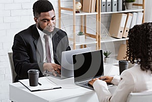 Young black man working with his female colleague, feeling bored, doing dull task at open space company office