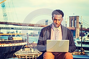 Young black man working on laptop computer ourdoors by river in New York City