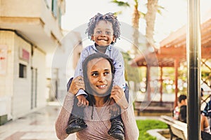 Young black mother and son together have fun and enjoy the playhood at the park  mommy take litthe boy on her shoulder - happiness