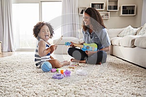 Young black mum plays ukulele with toddler daughter at home