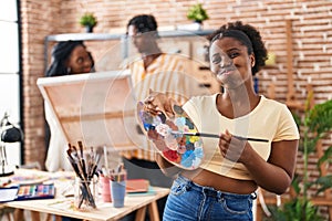 Young black painter woman at art studio holding palette puffing cheeks with funny face