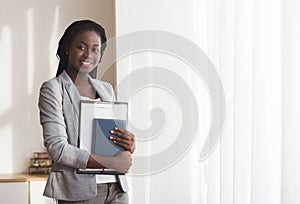 Young black secretary standing with clipboard and notebook in office