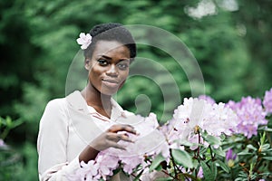 Young black woman with afro hairstyle in urban park. Afro american girl wearing casual clothes between purple flowers.