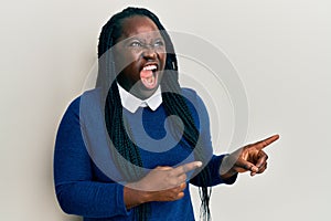 Young black woman with braids pointing up with fingers to the side angry and mad screaming frustrated and furious, shouting with