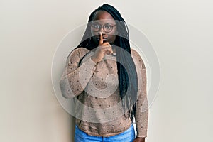 Young black woman with braids wearing casual clothes and glasses asking to be quiet with finger on lips