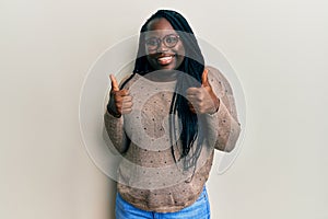 Young black woman with braids wearing casual clothes and glasses success sign doing positive gesture with hand, thumbs up smiling