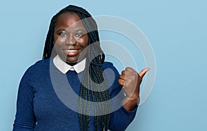Young black woman with braids wearing casual clothes smiling with happy face looking and pointing to the side with thumb up