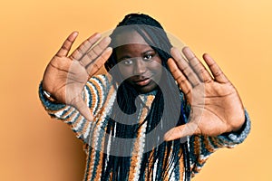 Young black woman with braids wearing casual winter sweater doing frame using hands palms and fingers, camera perspective