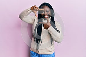 Young black woman with braids wearing casual winter sweater smiling making frame with hands and fingers with happy face