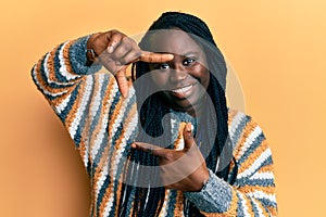 Young black woman with braids wearing casual winter sweater smiling making frame with hands and fingers with happy face