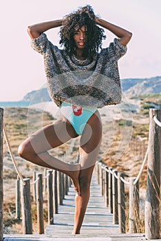 Young black woman doing yoga in a wooden foot bridge by the beach
