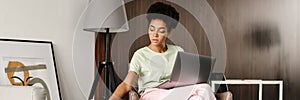 Young black woman drinking coffee working with laptop at home