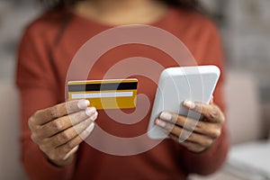 Young black woman holding credit card and using her smartphone at home